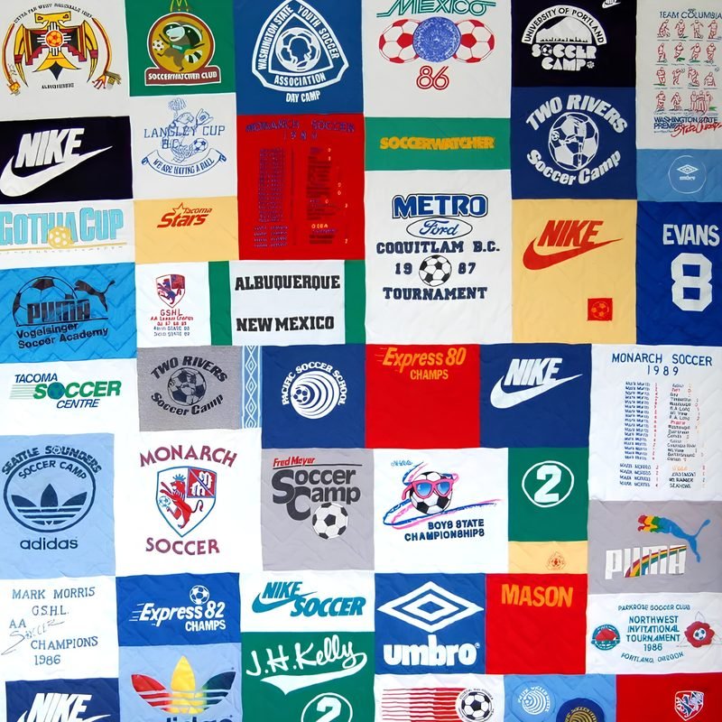 Hodgepodge-style T-shirt quilt by Rosie Rhine of Rhino Quilting, made of rectangular patches of different sizes, all from soccer shirts. The logos include Nike, Adidas, Puma, Umbro, Two Rivers Soccer Camp, Monarch Soccer, Seattle Sounders, and a “Mason” patch. The shirts are in white, red, blue, green, navy, and gray, and the patches fit together without a set pattern.