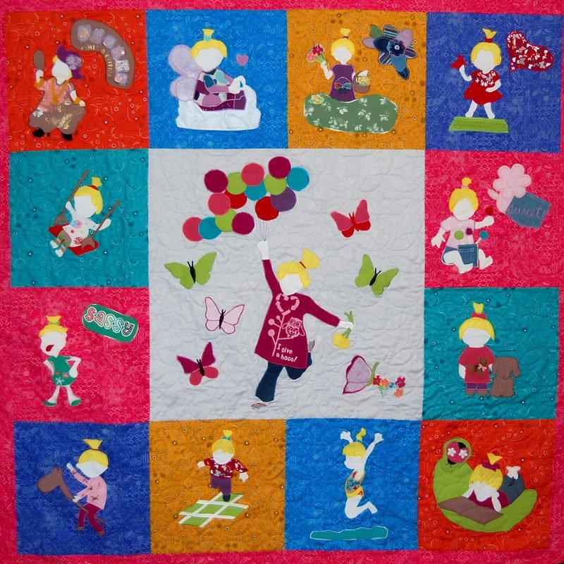 Appliqué memory quilt by Rosie Rhine of Rhino Quilting, with a large gray center panel framed by twelve smaller blocks in bright red, orange, blue, teal, and pink, all inside a hot pink border. In the center, a little girl in a maroon cardigan runs happily with a bunch of colorful balloons, surrounded by butterflies. In each of the surrounding blocks, the same girl, with blonde hair in a topknot, is shown in a different moment of play. She appears with fairy wings, holding a heart, picking flowers, swinging, riding a toy horse, playing hopscotch, jumping, and cuddling a teddy bear.