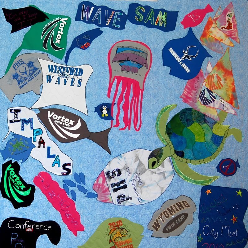 T-shirt quilt by Rosie Rhine of Rhino Quilting with a sea-blue background, where swim and water-themed shirt pieces are cut into shapes like fish, a jellyfish, a stingray, and other sea life. A large green sea turtle pieced from batik fabrics swims at the right. The shirt logos include Vortex, Westside Waves, Impalas, Wyoming Swim Camp, and PHS, along with the words “Wave” and “Sam.” Darker logos sit along the bottom like an ocean floor.
