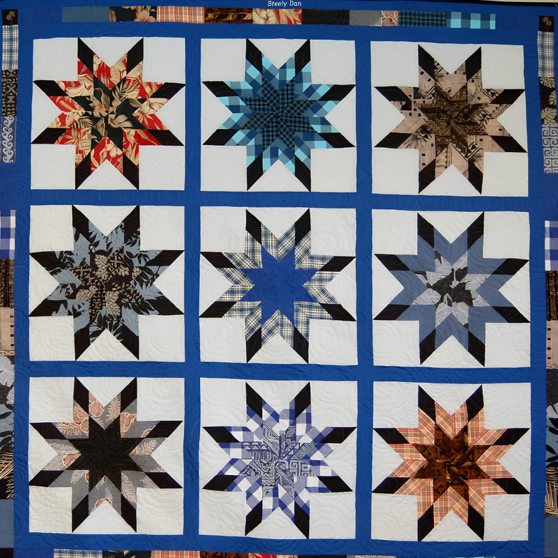 Square Lone Star quilt made by Rosie Rhine of Rhino Quilting. Nine eight-pointed stars are arranged in three rows of three, each with black points and a differently patterned center. Top row: red and black Hawaiian-style floral, turquoise and navy plaid, and tan and brown print. Middle row: black and gray floral, navy plaid around a solid blue center, and slate blue with gray prints. Bottom row: black and gray paisley, blue and white plaid, and orange and brown plaid. The stars are set on cream blocks framed by bright royal blue sashing, with a pieced border of mixed fabric strips around the edge. Swirling quilting stitches are visible across the cream backgrounds.