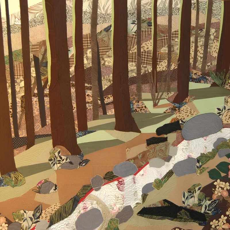 Pictorial art quilt by Rosie Rhine of Rhino Quilting showing a woodland scene. Tall brown tree trunks rise against a hazy background of tan and beige fabrics. A pale stream with white and pink water tumbles down a slope of brown, green, and tan ground, past gray boulders and small patches of leafy-print fabric.
