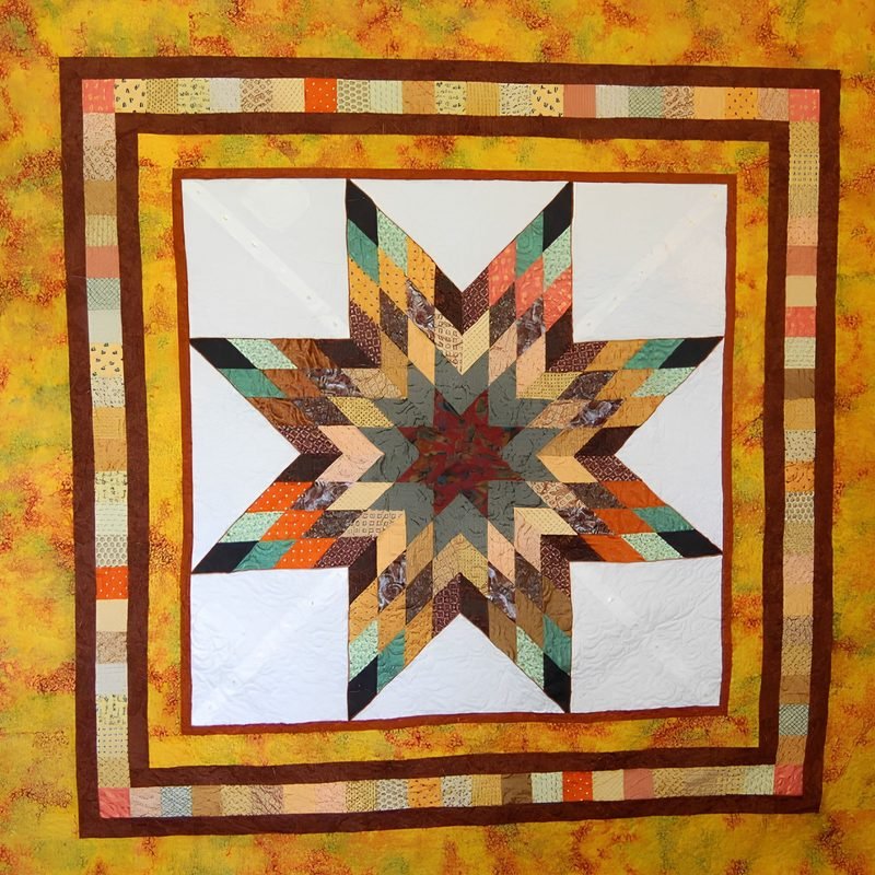 Lone Star quilt by Rosie Rhine of Rhino Quilting. A large eight-pointed star pieced from strips of teal, green, orange, tan, and rust fabrics, with a dark red center, sits on a white square with fine quilting lines. The square is framed by thin dark brown borders and a pieced border of small multicolored print strips. The outer background is a mottled gold and orange fabric.