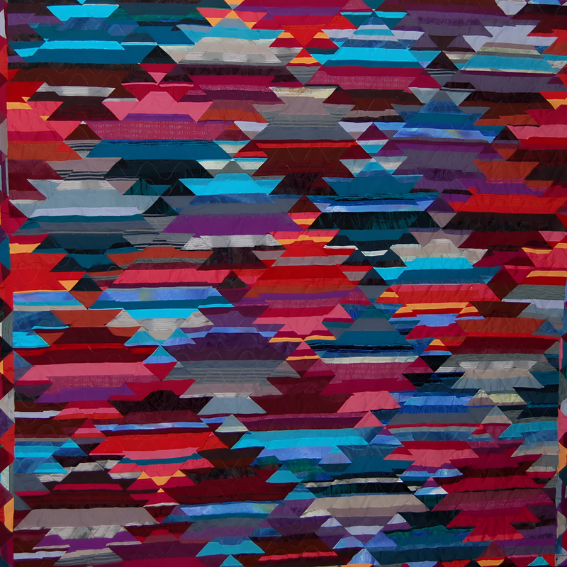 Contemporary quilt by Rosie Rhine of Rhino Quilting with a repeating kilim-style pattern of stepped diamonds and zigzag bands. The pattern is pieced in horizontal strips of red, crimson, magenta, purple, teal, turquoise, and gray fabrics, with dark navy and black shapes between the bands. The colors vary from strip to strip, so the surface looks woven.