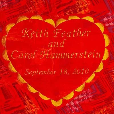 Close-up of a quilt label by Rosie Rhine of Rhino Quilting: a red heart with a scalloped gold edge on red fabric, embroidered in gold script with “Keith Feather and Carol Hammerstein, September 18, 2010.”